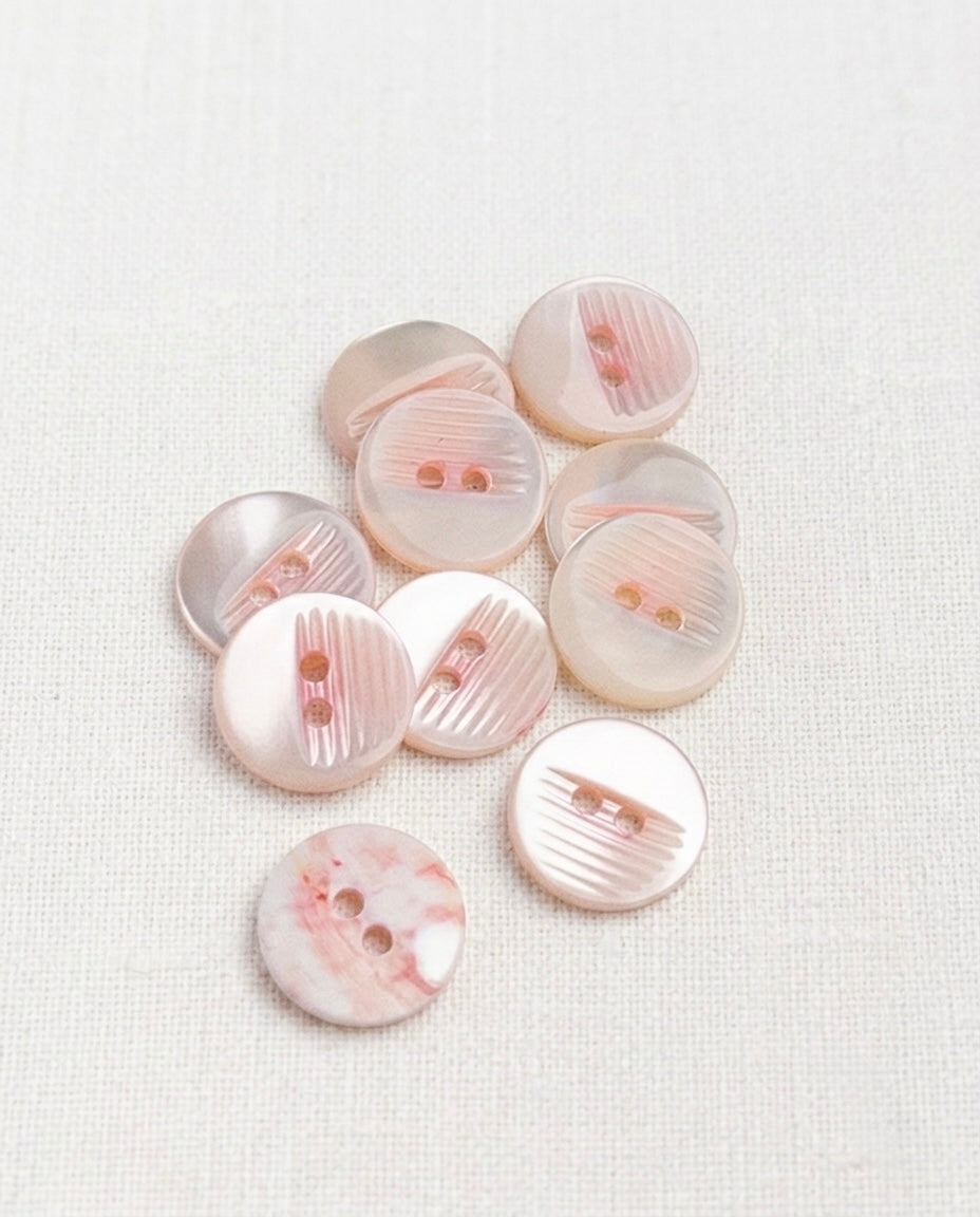 Neuf boutons ronds en nacre rosée de 15 mm à 2 trous, stries gravées en biais et reflets nacrés, dont un vu de dos