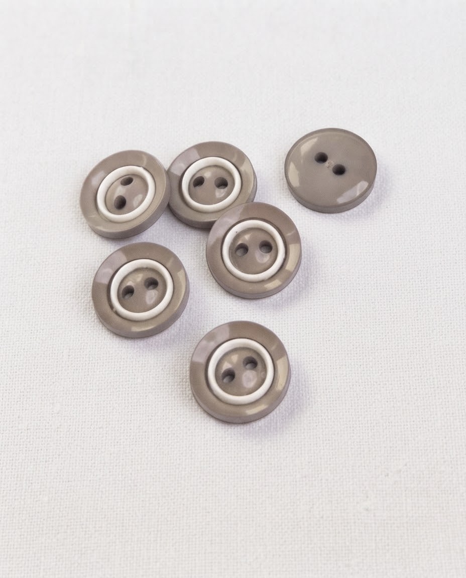 Boutons ronds gris taupe et blanc de 14 mm à 2 trous vus de dessus sur un tissu blanc, dont un vu de dos uni