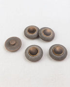 Boutons ronds gris mat et doré de 22 mm vus de biais sur une toile écrue, dont un retourné montrant sa queue