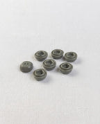 Petits boutons carrés gris vert de 12 mm vus de biais, relief carré autour des deux trous, sur un tissu blanc