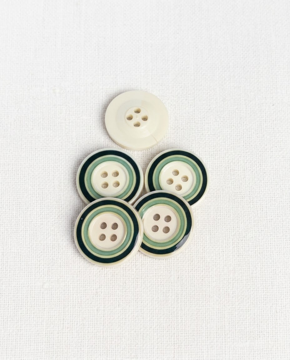 Boutons ronds crème à cercles verts de 22 mm à 4 trous posés sur un tissu blanc