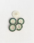 Boutons ronds crème à cercles verts de 22 mm à 4 trous posés sur un tissu blanc