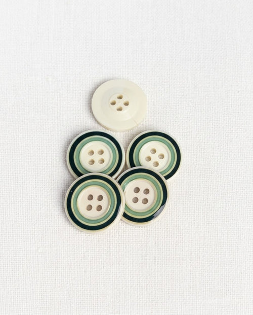 Boutons ronds crème à cercles verts de 22 mm à 4 trous posés sur un tissu blanc