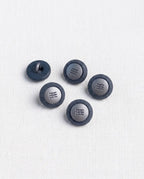 Boutons bleu jean à centre argenté de 14 mm vus de dessus sur un tissu blanc, avec un bouton retourné pour voir sa queue
