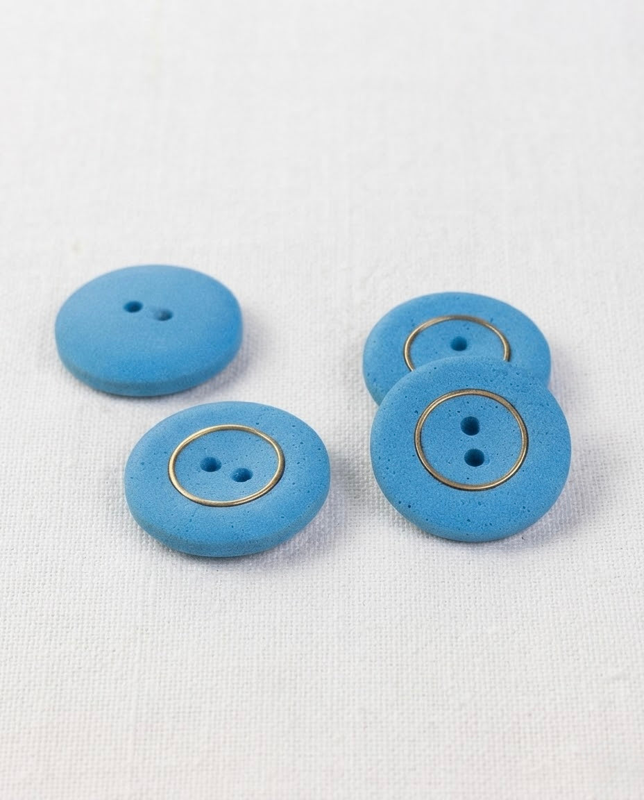 Vue de biais de quatre boutons bleus de 22 mm à 2 trous avec anneau doré