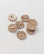 Huit boutons ronds beige taupe de 15 mm à 2 trous, gravés de rayons en forme de soleil, dont un vu de dos lisse et nacré