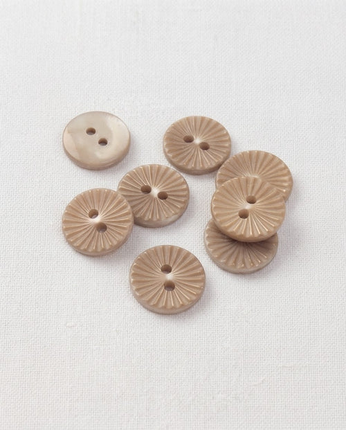 Huit boutons ronds beige taupe de 15 mm à 2 trous, gravés de rayons en forme de soleil, dont un vu de dos lisse et nacré