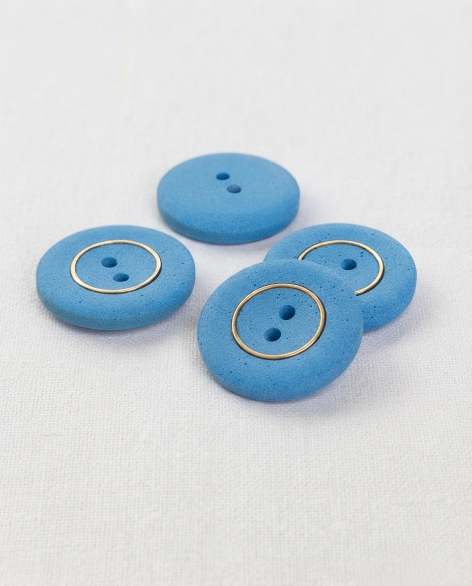 Quatre grands boutons ronds bleu mat de 22 mm à 2 trous, trois cerclés d'un anneau doré et un vu de dos