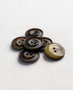 Boutons ronds vert olive de 22 mm à 2 trous posés en tas, un bouton retourné montre son dos plus clair