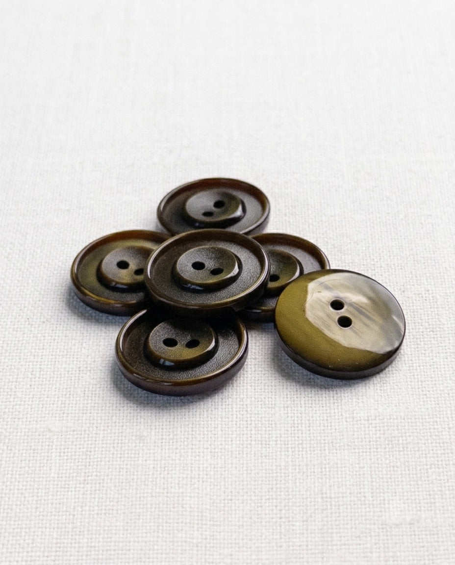 Boutons ronds vert olive de 22 mm à 2 trous posés en tas, un bouton retourné montre son dos plus clair