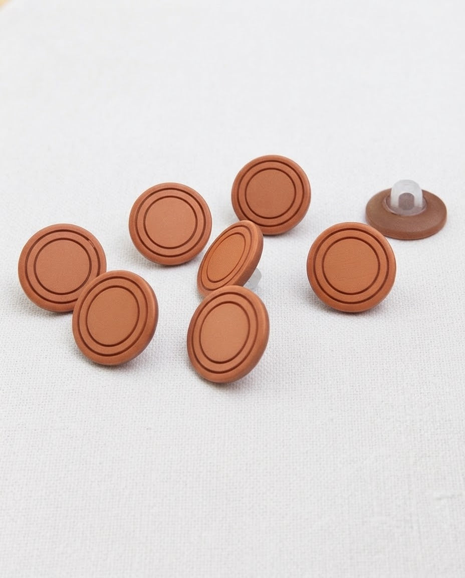 Boutons terre cuite de 15 mm à queue vus de biais sur une toile blanche, un bouton retourné montre sa queue
