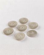 Sept boutons ronds beige grisé mat de 15 mm à 2 trous, centre creusé cerné de deux cercles, vus de biais