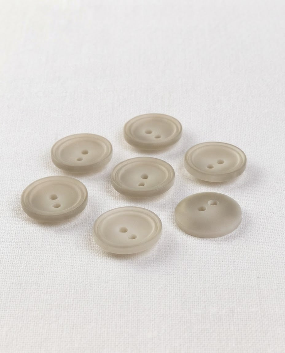 Sept boutons ronds beige grisé mat de 15 mm à 2 trous, centre creusé cerné de deux cercles, vus de biais