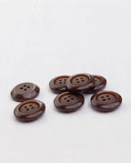 Sept boutons marron chocolat de 17 mm à 4 trous posés sur une toile blanche, dont un retourné