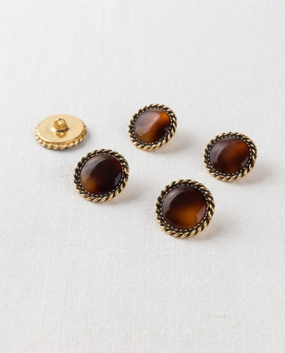 Boutons ronds à centre caramel et cordon doré tressé de 19 mm, vus de biais sur un tissu blanc