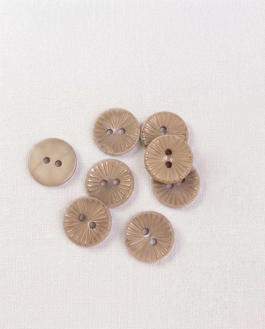 Gros plan sur des boutons fins beige taupe de 15 mm à 2 trous, leurs rayons gravés et un bouton retourné