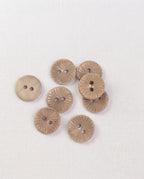 Gros plan sur des boutons fins beige taupe de 15 mm à 2 trous, leurs rayons gravés et un bouton retourné