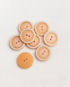 Boutons pêche et doré de 18 mm à 2 trous vus de dessus, le filet doré souligne le bord crème