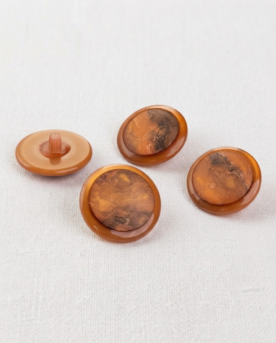 Quatre grands boutons ronds cuivre de 22 mm à queue, bord caramel et centre marbré brun et orange, dont un vu de dos