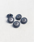 Cinq boutons ronds bleu jean de 14 mm à queue, bord mat granuleux et centre argenté gravé de lignes, dont un retourné qui montre la queue en métal