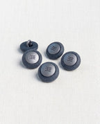 Cinq boutons ronds bleu jean de 14 mm à queue, bord mat granuleux et centre argenté gravé de lignes, dont un retourné qui montre la queue en métal