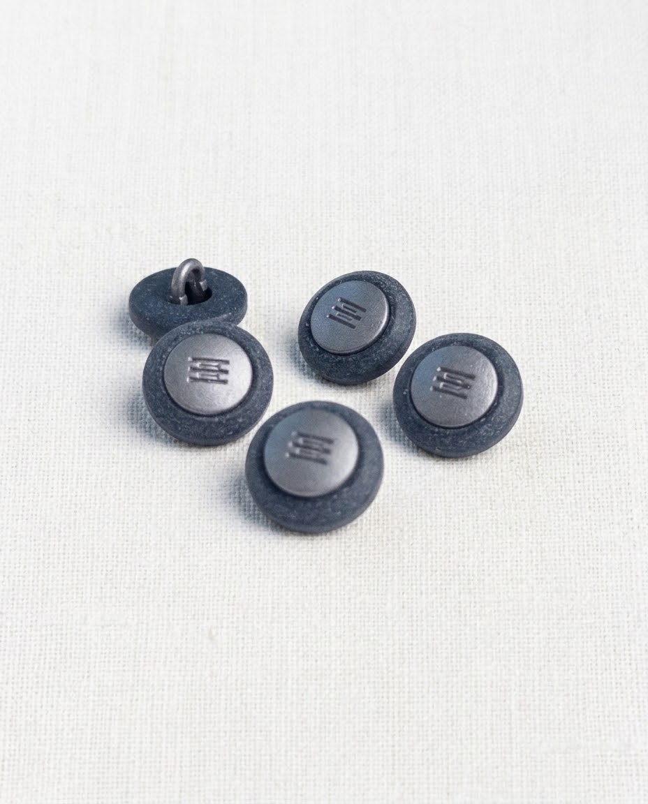 Cinq boutons ronds bleu jean de 14 mm à queue, bord mat granuleux et centre argenté gravé de lignes, dont un retourné qui montre la queue en métal