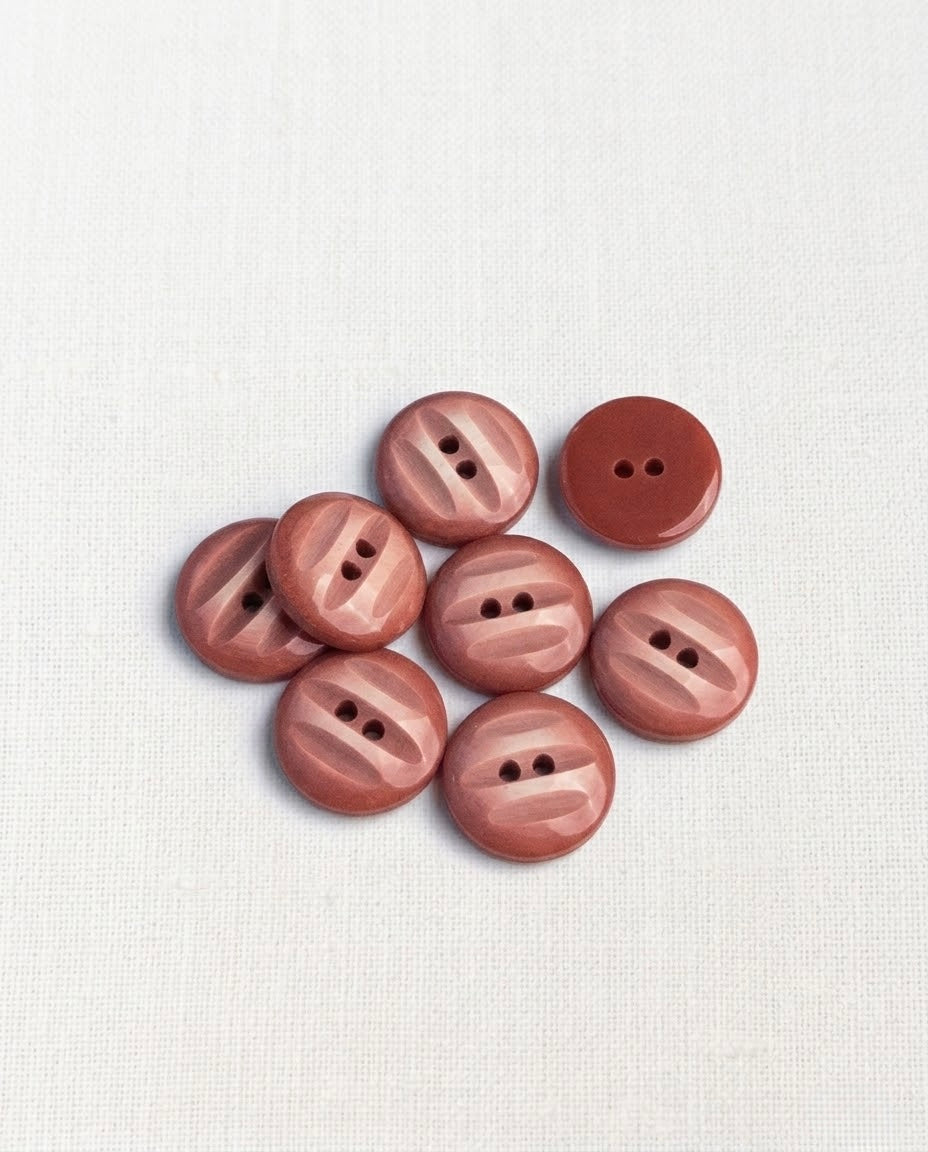 Boutons ronds rose brique de 12 mm à 2 trous vus de dessus sur un tissu blanc, un bouton retourné uni