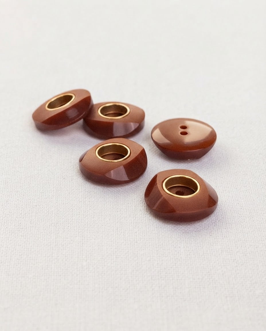 Boutons marron et doré de 18 mm posés de trois quarts, les facettes et l'anneau doré accrochent la lumière