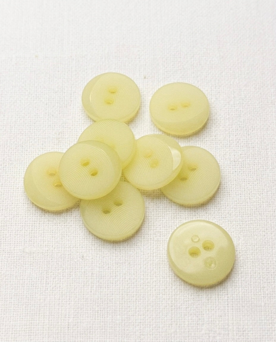 Une dizaine de boutons ronds jaune pâle translucides de 18 mm à 2 trous, surface finement striée, dont un vu de dos