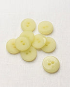 Une dizaine de boutons ronds jaune pâle translucides de 18 mm à 2 trous, surface finement striée, dont un vu de dos
