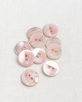 Neuf boutons ronds en nacre rosée de 15 mm à 2 trous, stries gravées en biais et reflets nacrés, dont un vu de dos