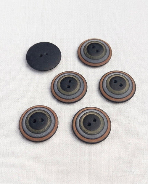 Boutons à cercles noir, kaki, gris et cuivre de 23 mm posés sur un tissu blanc, avec un bouton retourné