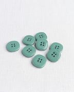 Huit boutons carrés vert de gris de 17 mm à 4 trous vus de dessus, dont un retourné