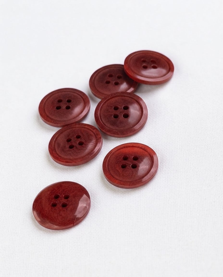 Boutons ronds rouge brique de 17 mm à 4 trous posés sur une toile écrue, marbrures plus foncées