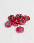 Huit boutons ronds fuchsia brillants de 14 mm à 2 trous avec un insert doré au centre, dont un vu de dos rose uni
