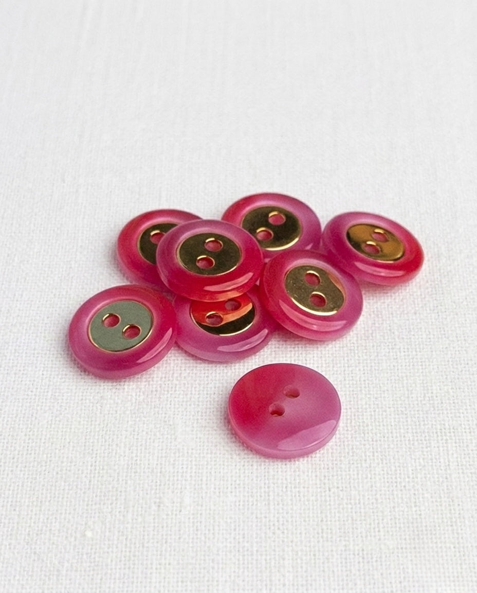 Huit boutons ronds fuchsia brillants de 14 mm à 2 trous avec un insert doré au centre, dont un vu de dos rose uni