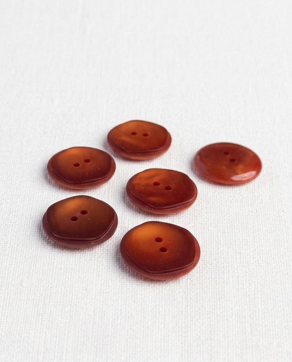 Boutons ronds rouille ambré de 21 mm à 2 trous posés sur une toile écrue, reflets chauds
