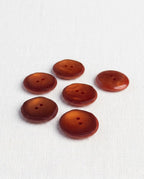 Boutons ronds rouille ambré de 21 mm à 2 trous posés sur une toile écrue, reflets chauds