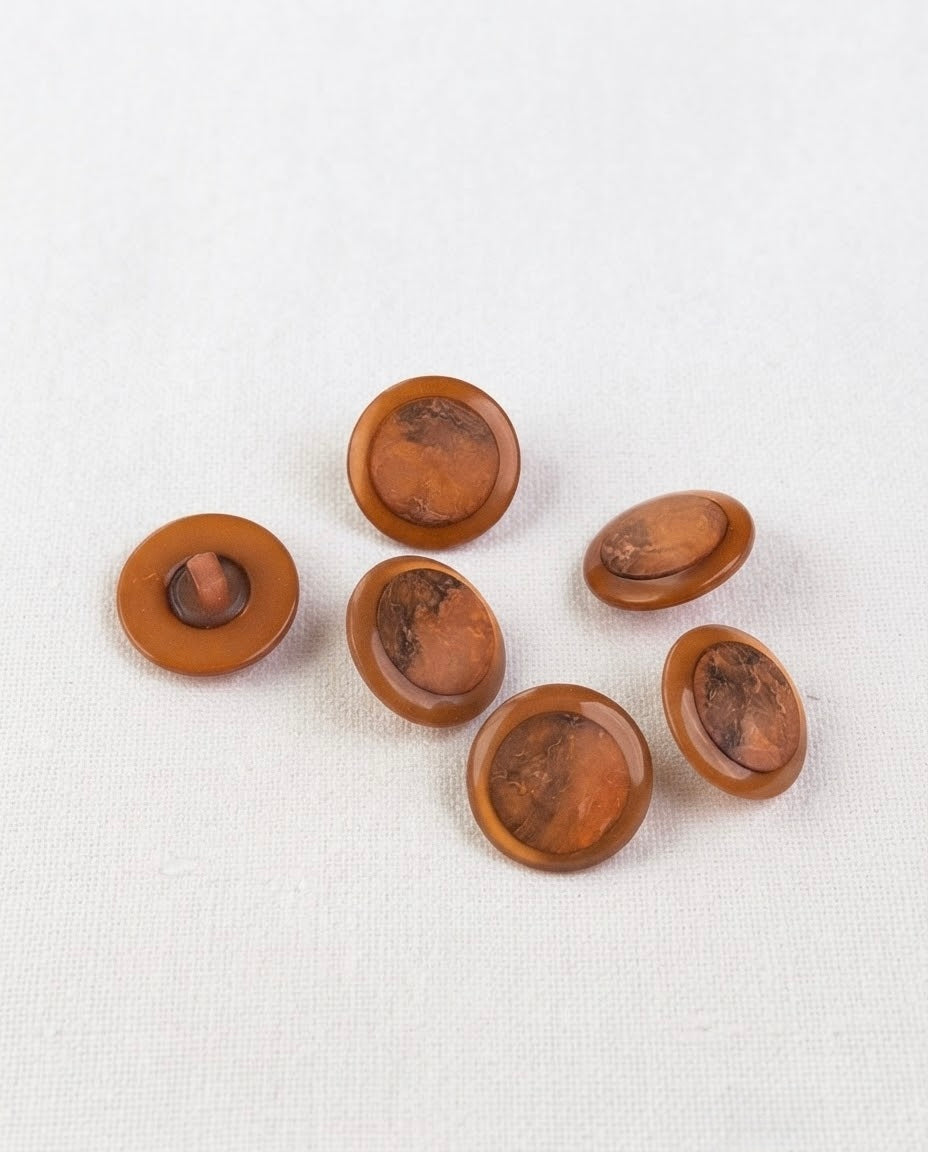 Boutons ronds cuivre de 17 mm vus de biais, un bouton retourné qui montre sa queue
