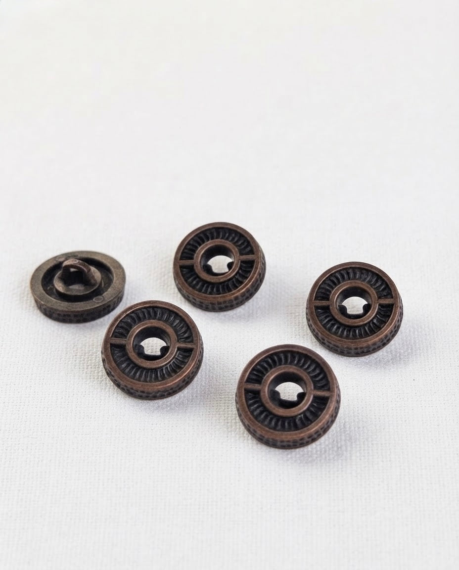 Boutons effet bronze sombre de 15 mm vus de biais, tranche perlée et face gravée, un bouton retourné montre sa queue