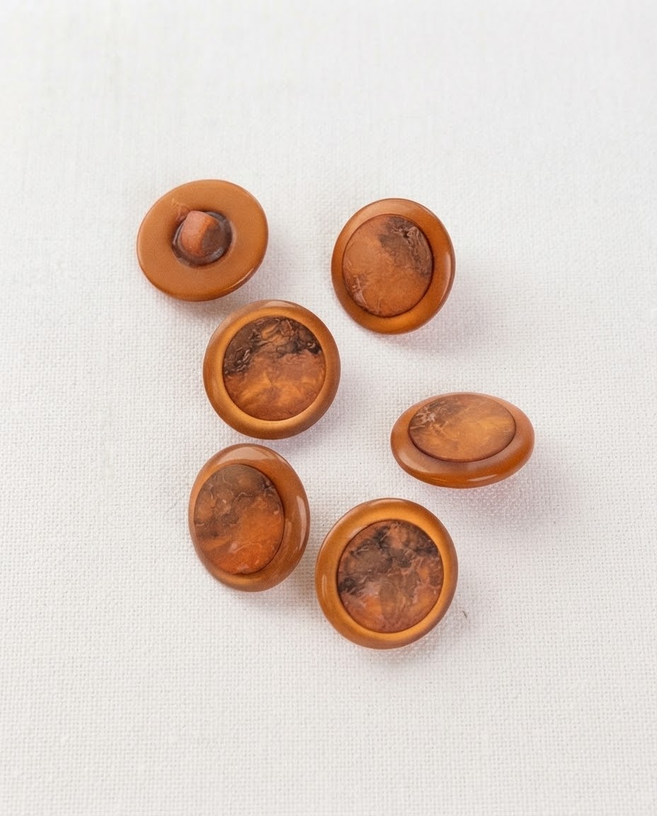 Boutons cuivre à centre marbré de 17 mm vus de dessus sur un tissu blanc, chaque marbrure différente