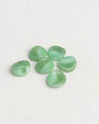 Boutons vert amande au bord ondulé de 15 mm posés sur une toile écrue, reflets marbrés