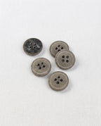 Boutons ronds gris kaki mouchetés de 15 mm à 4 trous vus de dessus sur un tissu blanc, dont un retourné