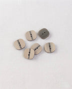 Boutons carrés beige et gris de 13 mm à 2 trous posés sur un tissu blanc, la surface à moitié lisse et à moitié striée