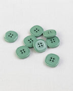 Petits boutons carrés vert de gris de 13 mm à 4 trous posés sur une toile écrue