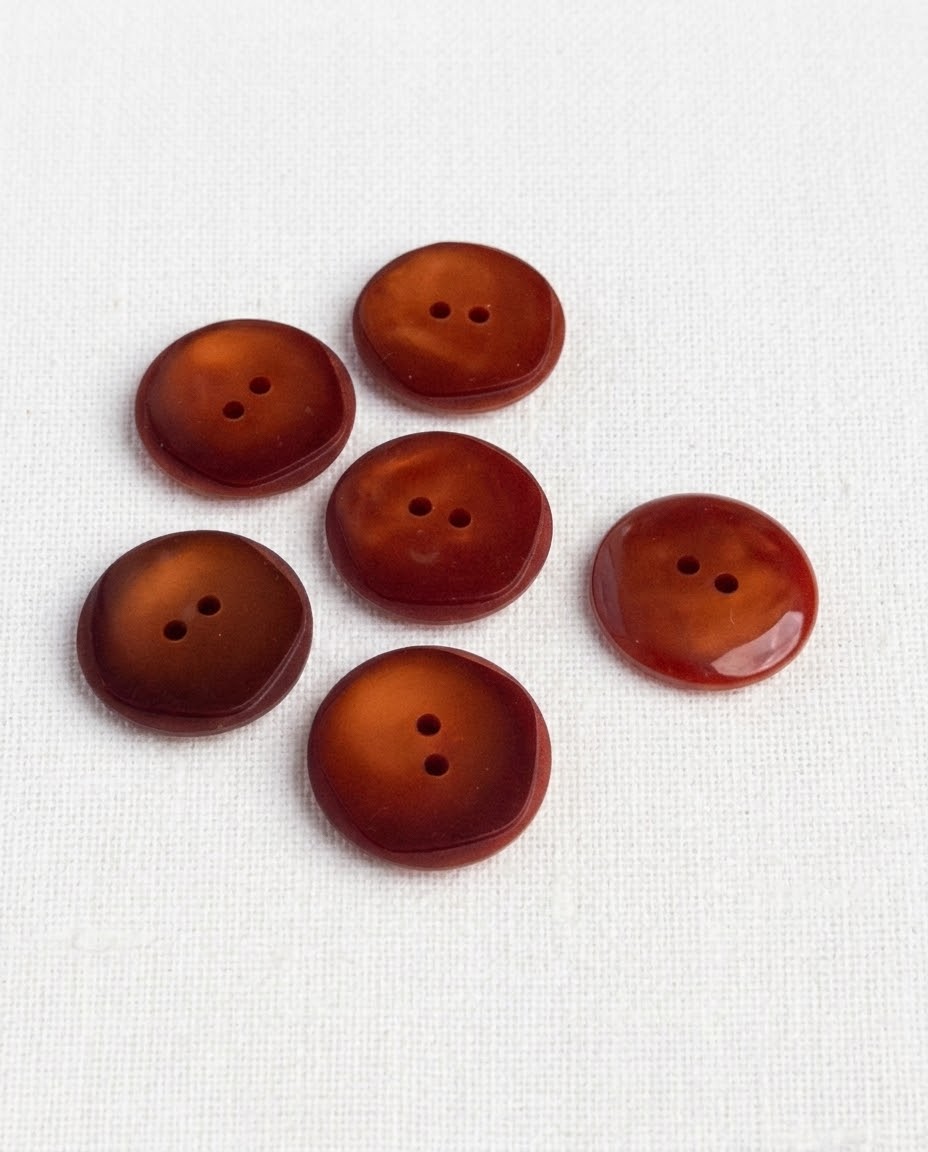 Six boutons rouille ambré de 21 mm à 2 trous vus de dessus, un bouton retourné montre son dos brillant