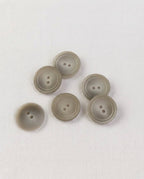 Boutons ronds effet corne beige grisé de 17 mm vus de dessus sur un tissu blanc, un bouton retourné