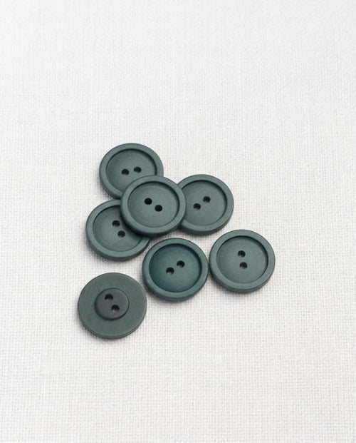 Boutons ronds bleu pétrole mat de 19 mm à 2 trous regroupés sur un tissu blanc, un bouton retourné au premier plan