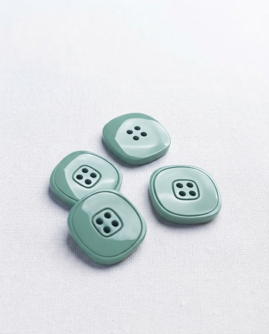 Boutons carrés vert de gris de 20 mm à 4 trous posés sur une toile écrue