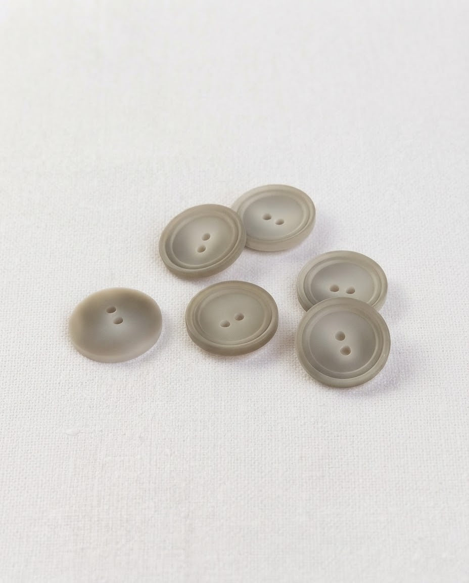 Boutons ronds beige grisé mat de 17 mm à 2 trous vus de biais, relief du centre bien visible